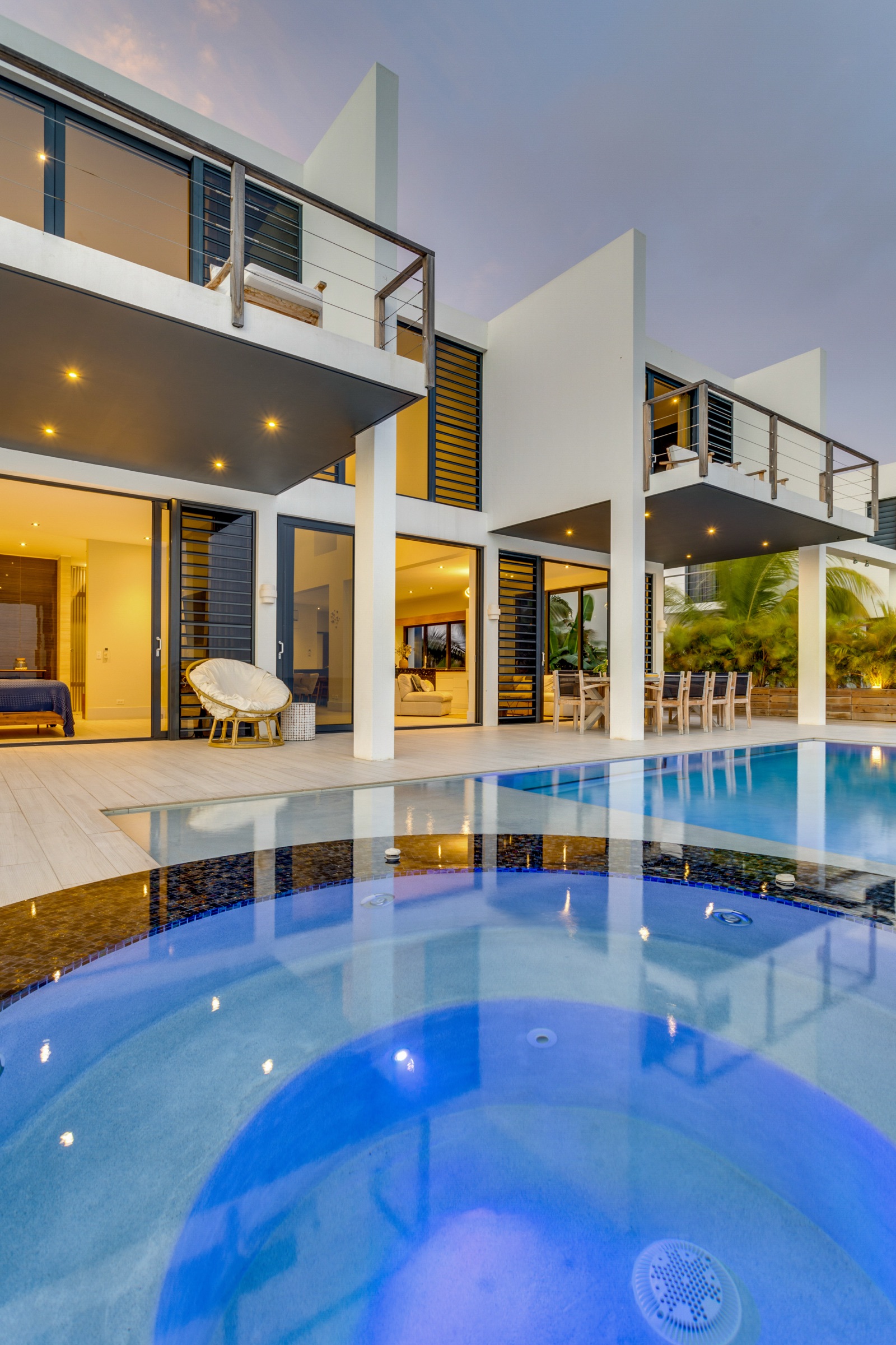 Luxury Bonaire villa exterior at dusk with a private illuminated pool and integrated jacuzzi, showcasing modern architecture and seamless indoor-outdoor living spaces.